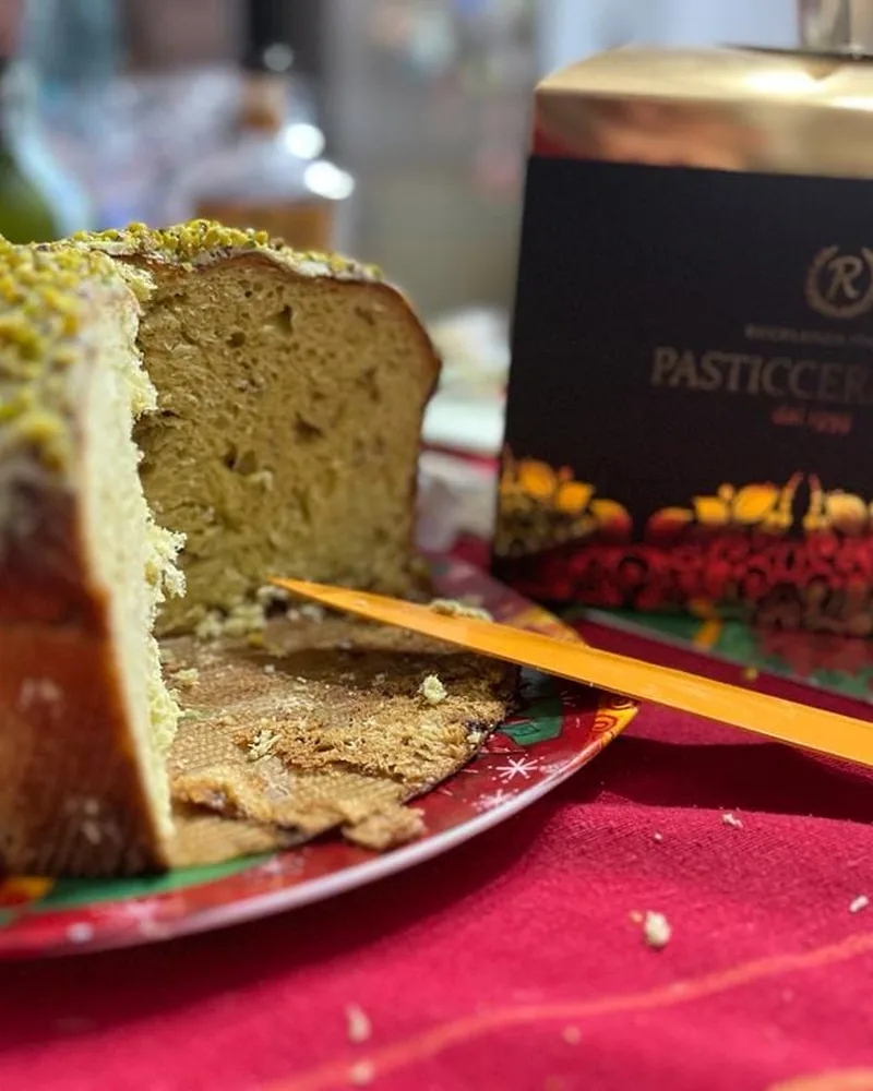 Panettone al pistacchio tagliato accanto alla scatola nera e oro della pasticceria